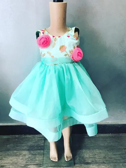A modern party frock for a two-year-old baby. This dress has a high-low hemline made with light organza fabric and 3D pink flowers attached to the bodice.