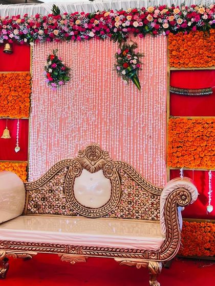 This Seemantham stage features a backdrop with panels of orange marigolds and a shimmering central curtain. The decor is accented with traditional waist belts (vaddanam) and hanging bells.