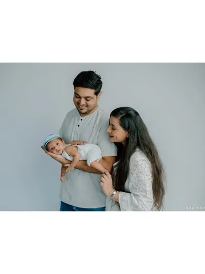 A slightly different pose from the same session shows the parents looking down at their little one, who is now awake and wearing an adorable cap. It’s these small variations that tell a fuller story.
