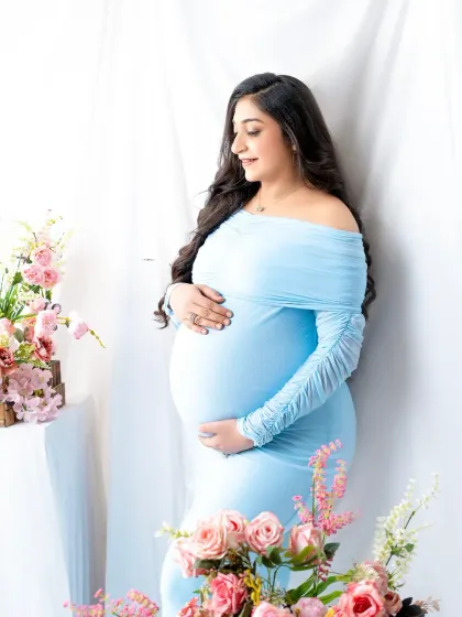 A serene portrait in powder blue. The mother-to-be is surrounded by soft pink flowers, creating a gentle and romantic color palette.