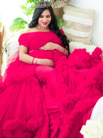 A stunning portrait featuring a vibrant magenta gown with a dramatic ruffled train. The mom-to-be is seated in our boho-chic setup, creating a look that is both regal and relaxed.