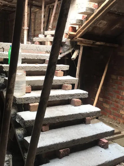A close-up of the raw concrete treads of a floating staircase during construction. The use of brick supports is temporary, part of the careful process of casting and curing such a delicate structural feature.