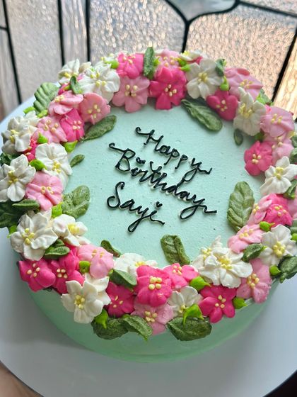 Another perspective of the "Happy Birthday Sayi" cake, showing the delicate arrangement of the buttercream flowers and leaves. We take care to make our cakes beautiful from every angle.
