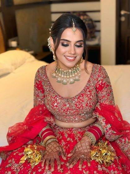The bride is all smiles, showing off her complete look. The floral bun adds a touch of freshness and softness to her traditional red bridal attire.