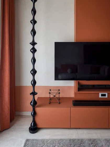 The TV wall unit features a striking glossy black wooden turning that runs from floor to ceiling, contrasting with the textured matte finish of the wall.