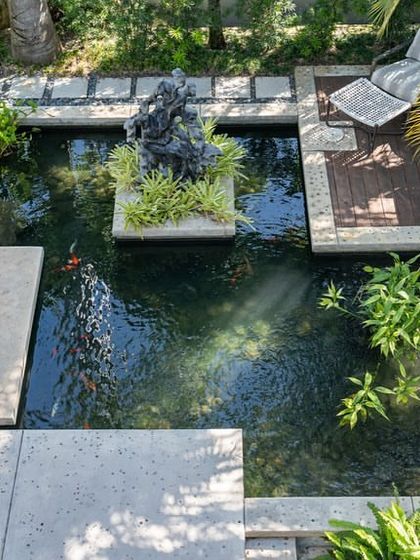 An overhead shot of a contemporary pond design. The geometric concrete slabs appear to float over the water, leading to a small deck and a central sculpture, showcasing our skill in complex hardscaping.