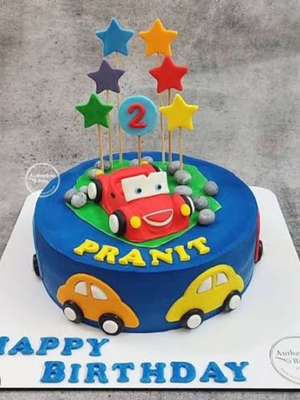 A cute car cake for a 2nd birthday, featuring a friendly red car character and colorful stars.