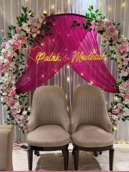 I can add a personal touch to your event with custom neon signs. This engagement backdrop features a circular floral arch with a beautiful sign showcasing the couple's names, "Palak & Madhav," making their special day even more memorable.