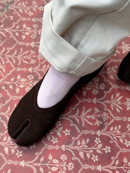 The rich texture of my brown suede DUPE Tabi flat, set against a traditional pattern. This shoe is about bringing together different worlds, creating a piece that feels both familiar and entirely new.