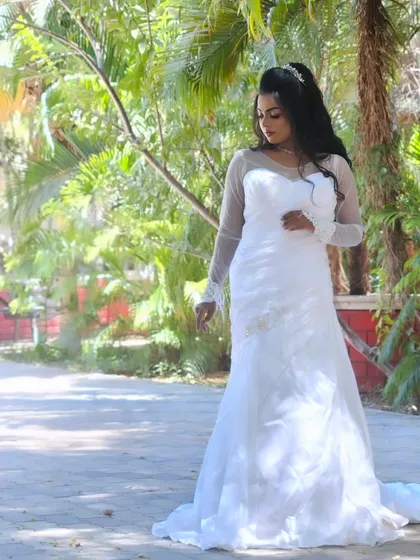 A full-length shot of a model in a white gown, posing gracefully in an outdoor setting. The makeup is natural and elegant.