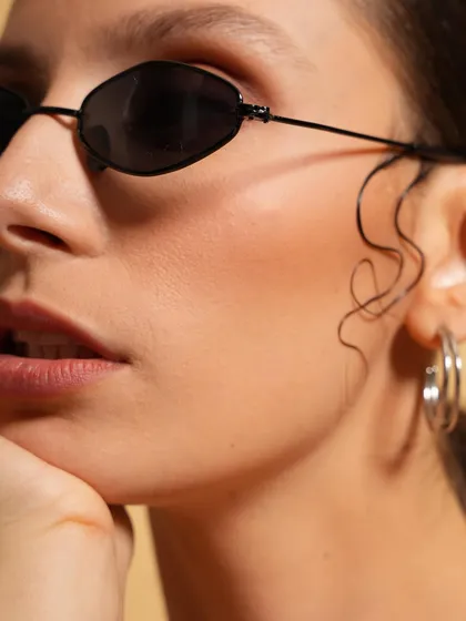 A modern beauty portrait focusing on the model's flawless skin and stylish sunglasses. The clean, warm background and the subtle hair styling create a chic and minimalist aesthetic.