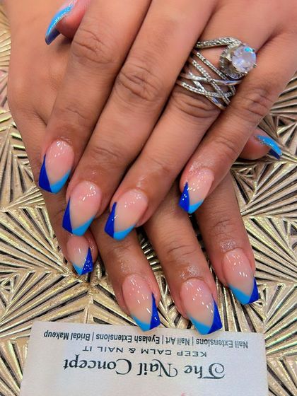 A bold and electric V-shaped French manicure. This design features a sheer nude base on square nails with vibrant blue V-tips for a striking, modern look.
