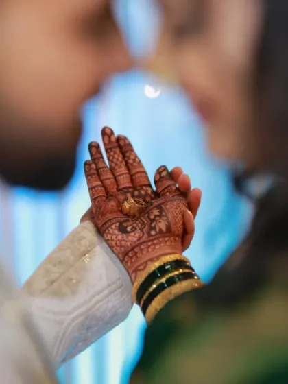 A romantic shot of an engagement couple. The focus is on the bride's hand, showcasing the beautiful henna stain and her engagement ring.