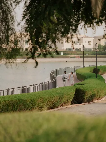 A beautifully framed shot of a couple walking along a lakeside path in a Dubai community. Using natural elements like trees to frame the shot adds depth and artistry.