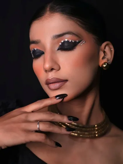 A dramatic pose with eyes closed, showcasing the intricate, sparkling eyeliner and the smooth, flawless makeup application.