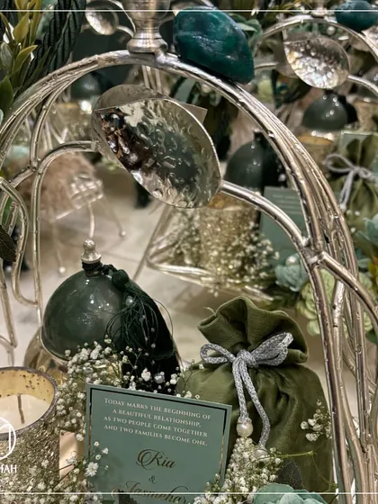 A detailed view of the Gilded Grove single-tier tray. Notice the silver-finished leaves, the green stone accents, and the soft velvet potli, all coming together to create a harmonious and luxurious wedding favor.
