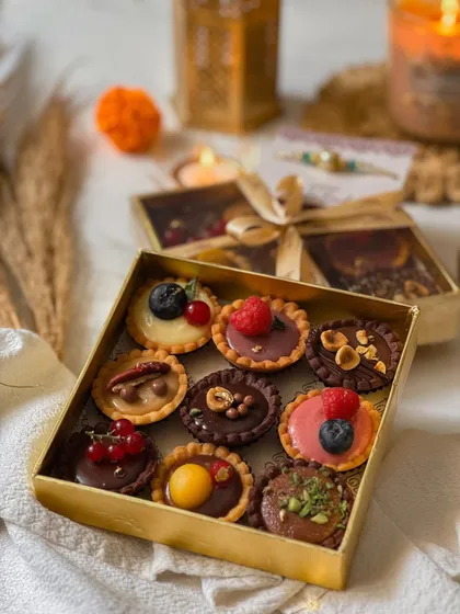 A golden box filled with nine assorted mini tartlettes, each topped with different fruits, nuts, and creams. The elegant packaging makes it a beautiful and delicious gift.