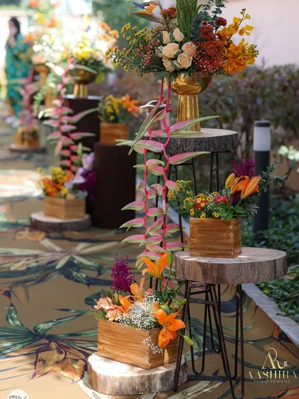 A beautiful floral-lined pathway with arrangements of tropical flowers in wooden boxes and gold vases, set on rustic wood slices.