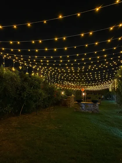 The farm lawn illuminated by a canopy of string lights at night. This simple yet stunning setup is perfect for any evening celebration.