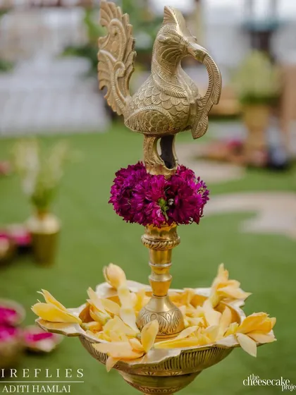 A traditional brass 'diya' (oil lamp) in the shape of a peacock, filled with yellow champa flowers. A beautiful and auspicious detail for a wedding ceremony.