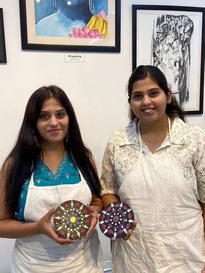 Two friends proudly hold up their finished dot mandala pieces. The vibrant colors and symmetrical patterns are mesmerizing.