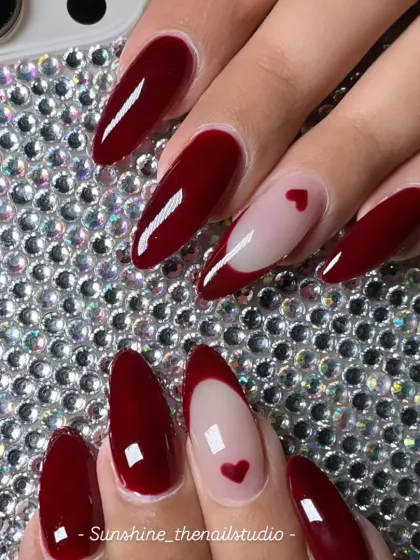 A classic with a twist. This set features long, almond-shaped nails in a deep, glossy red, with a couple of accent nails showing a negative space heart design for a romantic touch.