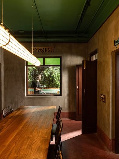 For this private dining room, I used earthy lime-washed walls and a dark red oxide floor to create a warm, grounded feeling. A long, custom wooden table sits under a modern tubular light, blending traditional materials with contemporary forms for a timeless appeal.