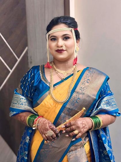 A traditional Maharashtrian bride ready for her wedding ceremony. She is wearing a yellow and blue saree with a Mundavalya and holding a decorative dagger.