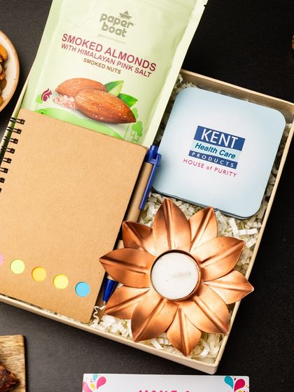 This hamper, featuring a branded tin from Kent Health Care, is a great example of co-branding. It includes smoked almonds, an eco-friendly notebook, and a copper flower diya, making it a practical and memorable corporate gift.