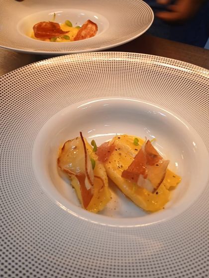 A delicate pasta dish featuring two pieces of agnolotti filled with a savory mixture, garnished with crispy prosciutto.