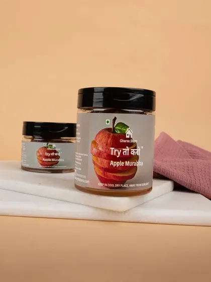 A styled shot of Apple Murabba jars, placed on a clean white marble slab with a textured cloth to create an appealing, homely feel for food products.