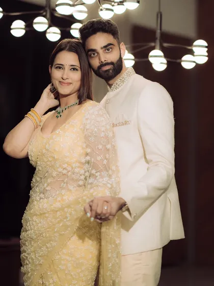 A classic, elegant portrait from an indoor engagement shoot. The couple holds hands, their pose exuding confidence and grace under the soft glow of a contemporary light fixture.