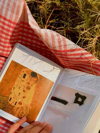 Reading a book on a picnic blanket, the pages glowing in the golden light of the setting sun.