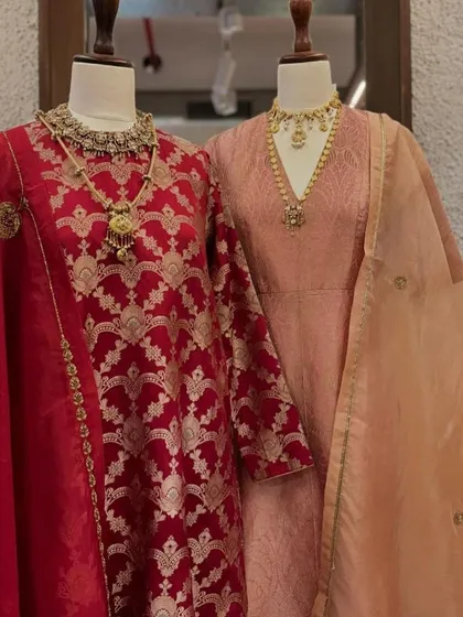 A full view of the red and peach Banarasi suits, highlighting the rich texture of the brocade and the elegant drape of the dupattas.