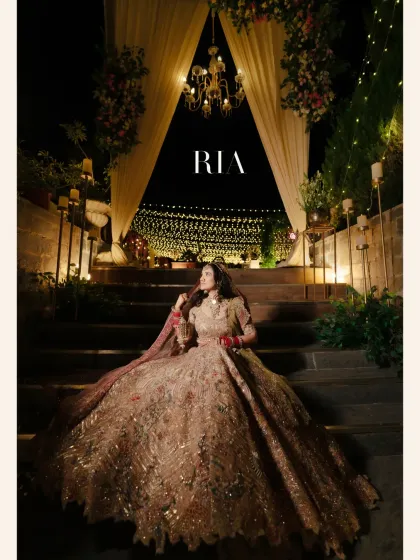 A grand, dramatic portrait of the bride seated on stairs, her magnificent lehenga taking center stage under a beautifully lit archway.