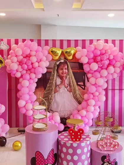 An adorable Minnie Mouse-themed fourth birthday party. This elaborate setup features large, pink, Minnie-shaped balloon sculptures, a striped backdrop, and a photo of the birthday girl.