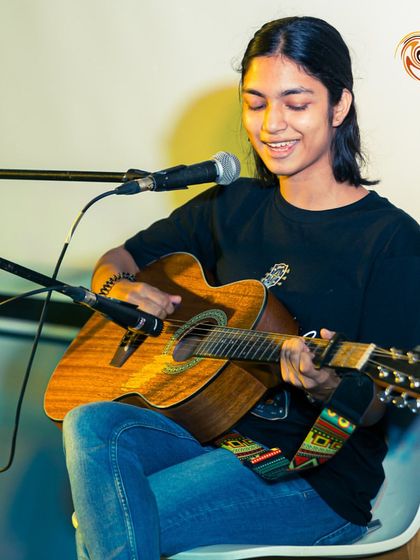 A student smiling as she plays her acoustic guitar during a Swirl Spotlight performance. We love seeing our students find joy in their music.