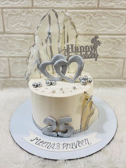 A sleek and modern silver anniversary cake celebrating 25 years. The design features silver hearts, abstract silver sails, and pearl details for a contemporary look.