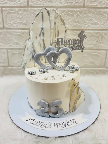 A sleek and modern silver anniversary cake celebrating 25 years. The design features silver hearts, abstract silver sails, and pearl details for a contemporary look.