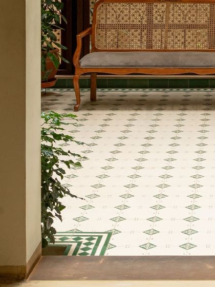 A quiet moment in the courtyard, featuring a classic cane bench against the backdrop of our signature patterned tiles. We design spaces that invite you to sit down and relax.