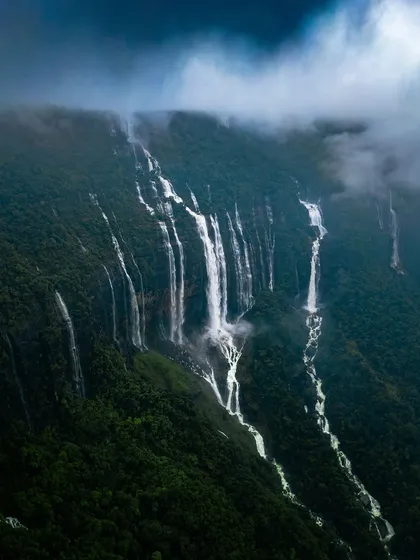 The Seven Sisters Falls shrouded in monsoon clouds, creating a mystical and dramatic landscape that feels otherworldly.