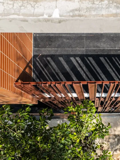 An aerial view showing the composition of textures: the terracotta-colored tiles, the dark flooring of the balcony, and the rhythmic pattern of the metal screen, all under the dappled light of the sun.