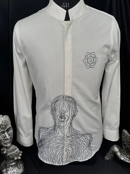 A full view of the minimalist white shirt with abstract figure embroidery. The mandarin collar and clean lines make it a powerful statement of contemporary style.