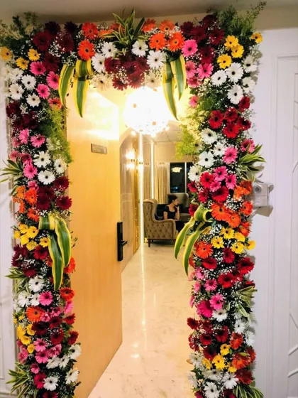 A beautiful floral frame for an apartment entrance. This design uses a mix of colorful gerberas and other seasonal flowers to create a full and vibrant archway, welcoming guests to the celebration.