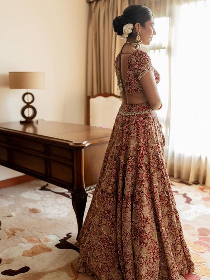 A full view of a bride in her room, her hair perfectly styled in a timeless bun.