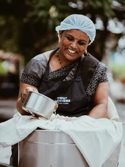A joyful portrait of a woman working at TBOF, smiling as she pours ghee. This shot captures the human element and the pride that goes into making the products.