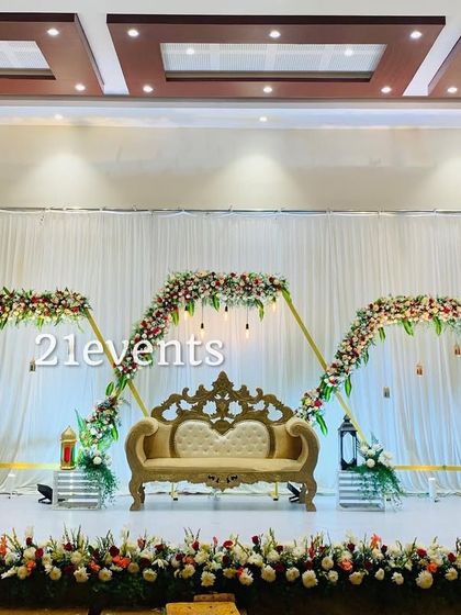 A grand and elegant stage setup for a formal celebration, featuring hexagonal arches adorned with flowers.