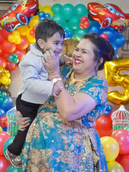 A joyful, candid moment between a grandmother and her grandson at his 5th birthday party. The colorful car-themed balloon decor adds to the festive atmosphere.