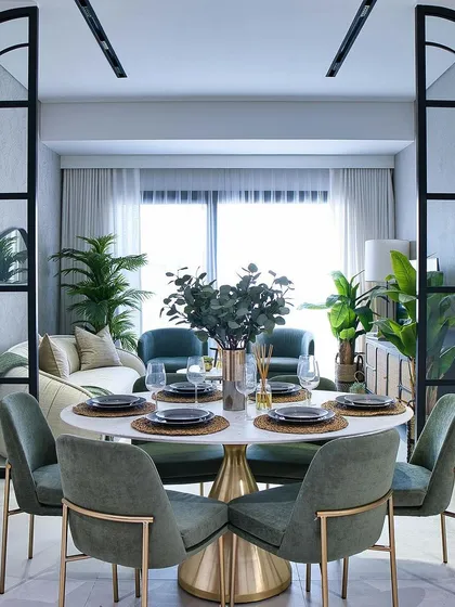 A sophisticated dining setup with plush green chairs around a marble-topped table, framed by elegant arched glass partitions.