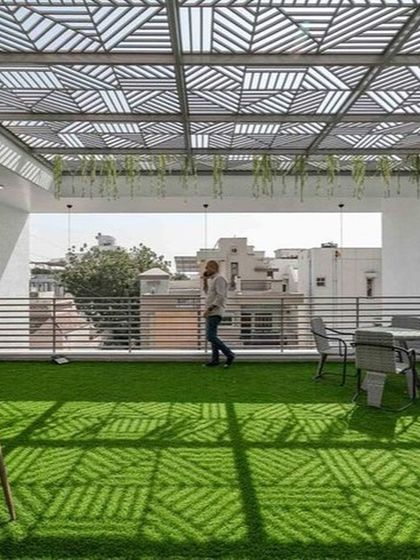 This rooftop terrace uses a stunning geometric-patterned pergola to create a dynamic play of light and shadow on the artificial turf below. It's a modern, spacious, and visually striking design perfect for gatherings.